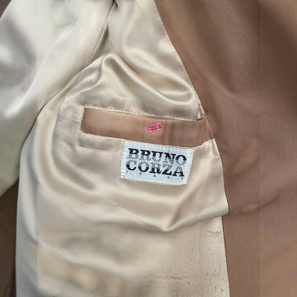 Etiqueta de marca Bruno Corza en el interior de una gabardina color marrón claro.